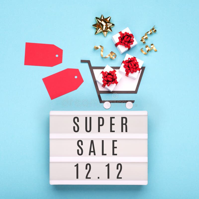 12.12 Super Sale text on white lightbox, shopping trolley, gift boxes and red tags on blue paper background. Double 12 Mega sales day concept. Top view, flat lay, copy space. 12.12 Super Sale text on white lightbox, shopping trolley, gift boxes and red tags on blue paper background. Double 12 Mega sales day concept. Top view, flat lay, copy space