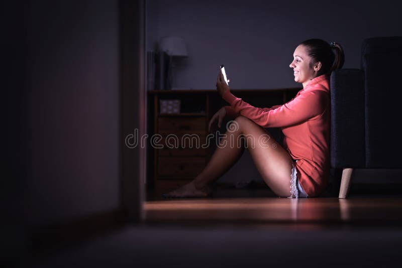 Textos da leitura da mulher com o smartphone na noite Pessoa de sorriso que usa o telefone celular Senhora feliz que data e que f fotografia de stock royalty free Textos da leitura da mulher com o smartphone na noite Pessoa de sorriso que usa o telefone celular Senhora feliz que data e que f fotografia de stock royalty free