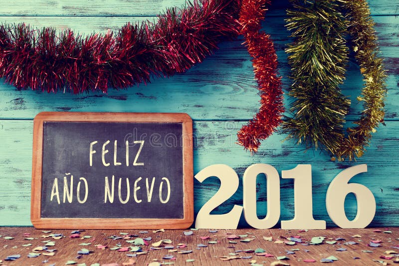 Tinsel of different colors and a chalkboard with the text feliz ano nuevo, happy new year in spanish, and white numbers forming the number 2016, on a rustic wooden surface sprinkled with confetti. Tinsel of different colors and a chalkboard with the text feliz ano nuevo, happy new year in spanish, and white numbers forming the number 2016, on a rustic wooden surface sprinkled with confetti