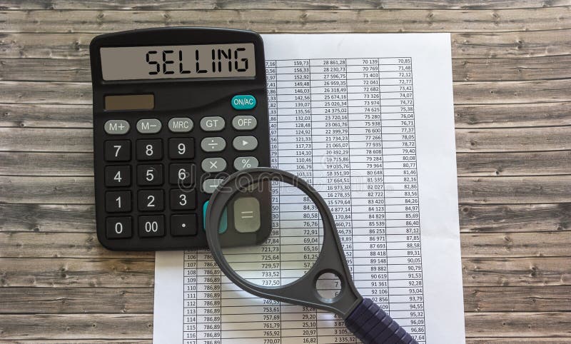 Textul pentru vânzarea scrisă pe un calculator de lângă o lupă amplificatoare și raportează în cifre pe o masă din lemn