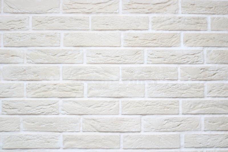 Texture of light beige scratched relief brick wall with white seams and rectangular bricks from decorative plaster.