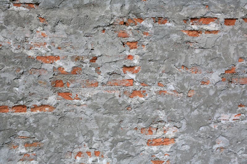 A textured, distressed wall surface showing a worn grey cement overlay partially revealing the underlying red brickwork, serving royalty free stock image