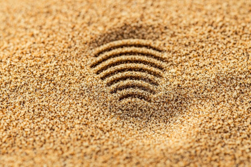 A textured pattern of concentric lines is imprinted in a sandy surface, resembling sound waves or ripples.