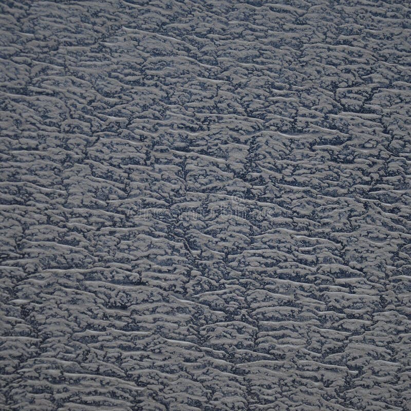 Gray sandy dirt on a black background. Textured surface showing a layer of fine, gray sandy particles on a darker, nearly black background. The sand creates a pattern of irregular, slightly raised formations, spaced closely together. The overall effect is a contrast between the lighter, gritty material and the underlying smoother, dark surface, creating an abstract and earthy visual texture. The image highlights the intricate details and natural randomness of the sandy arrangement.