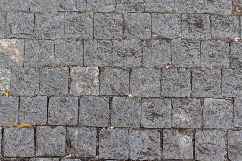 The textured surface of the sidewalk, square smooth gray stones, paving pavement. Backdrop texture background