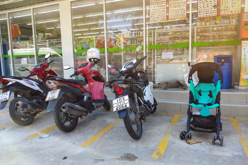 Thailand, Phuket - February 23, 2019: Motorcycle parking and a baby stroller in a parking space in front of the store. Baby rides stock photo Thailand, Phuket - February 23, 2019: Motorcycle parking and a baby stroller in a parking space in front of the store. Baby rides stock photo