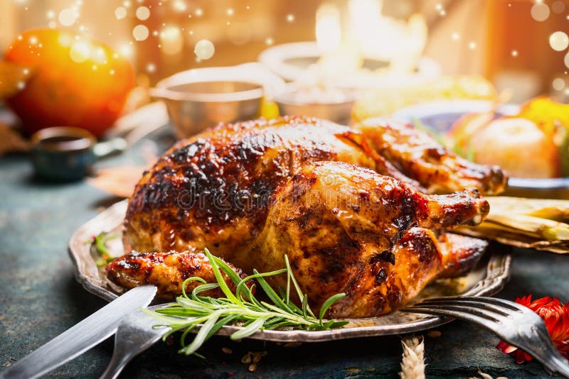 Thanksgiving day dinner table setting with whole roasted turkey or chicken on plate with cutlery , festive lighting and decoration, close up