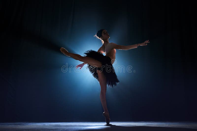 Theatrical performance. Beautiful, tender, graceful ballerina dancing against dark blue background with spotlight