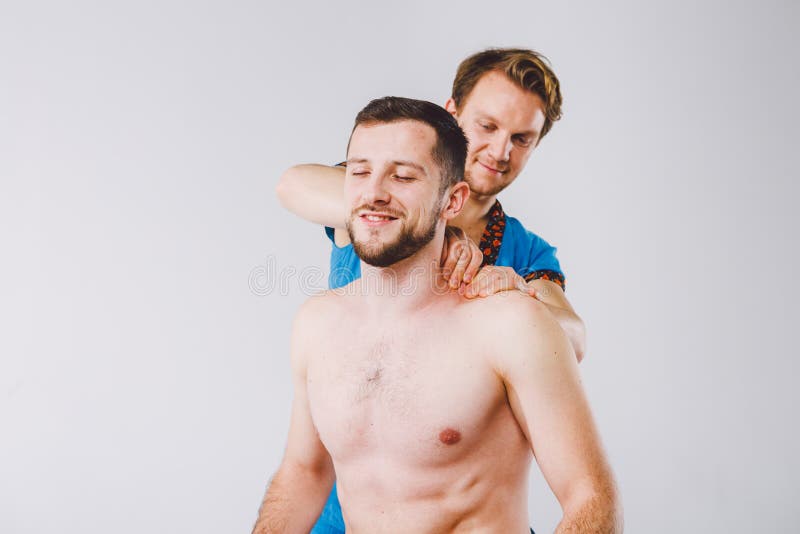 Themamassage en lichaamsverzorging Een knappe Kaukasische mannelijke arts in blauwe eenvormig en baard die spieren van hals en sc stock foto's Themamassage en lichaamsverzorging Een knappe Kaukasische mannelijke arts in blauwe eenvormig en baard die spieren van hals en sc stock foto's