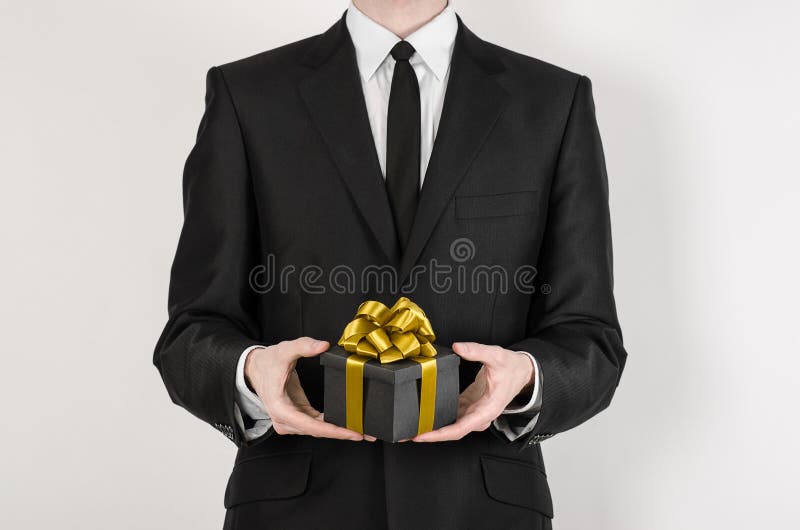 Theme holidays and gifts: a man in a black suit holds exclusive gift wrapped in a black box with gold ribbon and bow isolated on royalty free stock photos Theme holidays and gifts: a man in a black suit holds exclusive gift wrapped in a black box with gold ribbon and bow isolated on royalty free stock photos