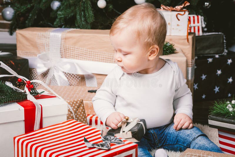 Theme winter and Christmas holidays. Child boy Caucasian blond 1 year old sitting home floor near Christmas tree with New Year dec