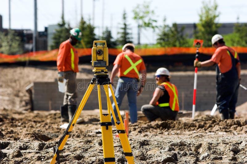 Theodolite on a tripod with construction workers in the background.