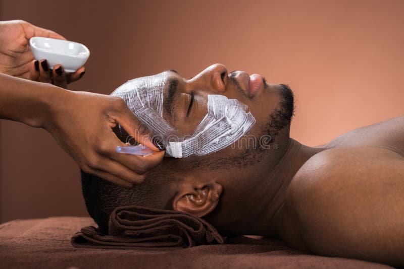 Therapist Applying Face Mask To Young African Man In Spa. Therapist Applying Face Mask To Young African Man In Spa