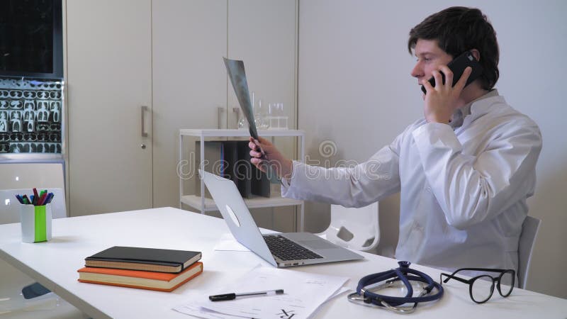 Therapist holding x-ray talking by mobile phone.