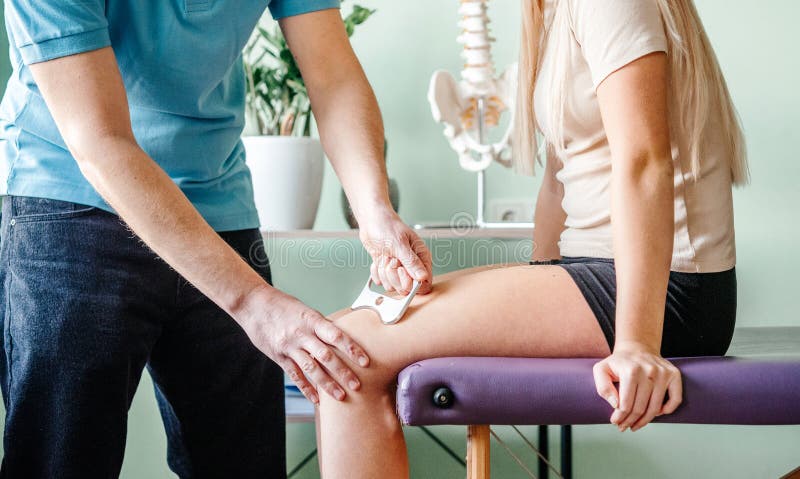 Therapist using IASTM instrument for soft tissue treatment on the leg of a female patient royalty free stock image