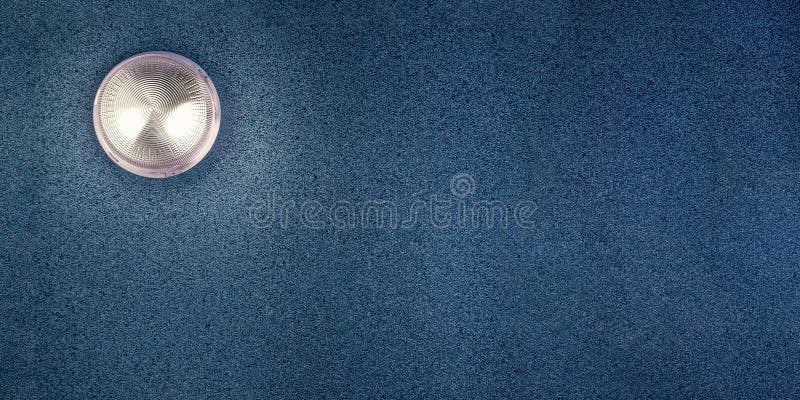 There is a lamp shining on the blue plastered wall, in the upper left corner. Monochrome abstract background with glowing lamp.