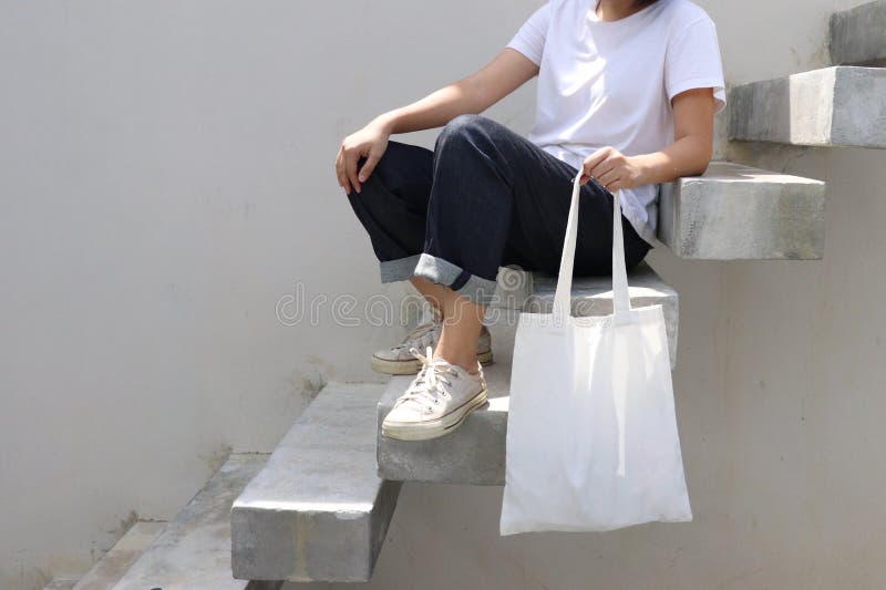 THERE IS model hold blank white fabric tote bag for save environment on street fashion with white t-shirt