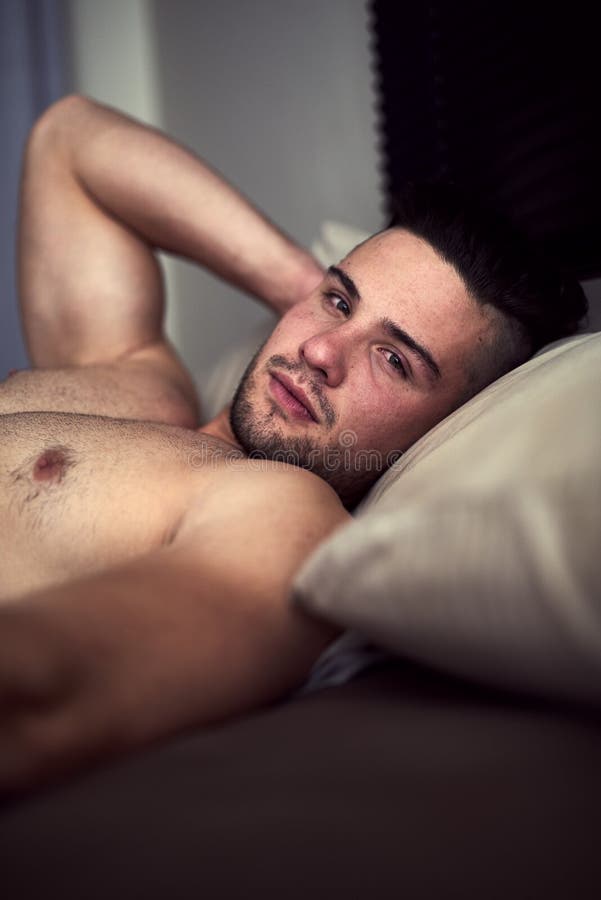 Theres room for one more in this bed. Portrait of a shirtless young man giving an inviting look while lying in bed. royalty free stock photography