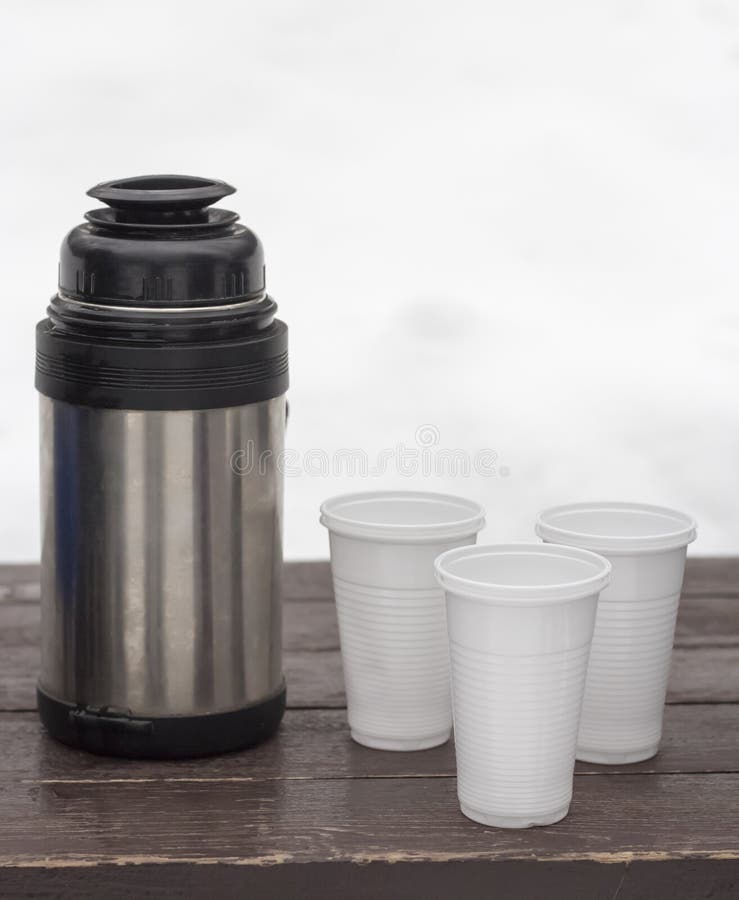 Thermos with Hot Tea and a Disposable Glass in Winter in a Snowdrift in