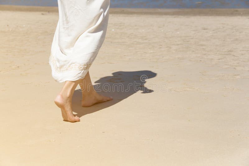The​ Low angle behind woman walking barefoot on beach stock image