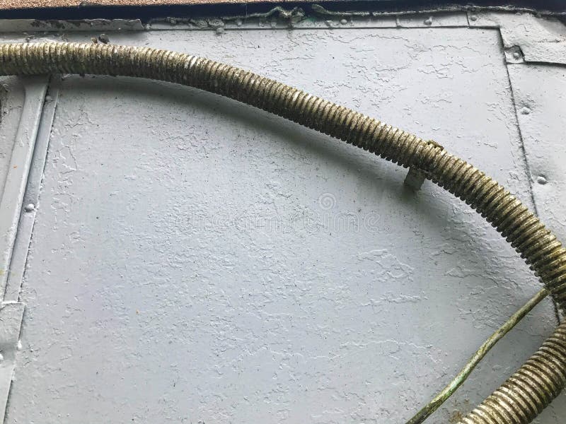 Thick gray-green wires hang from a gray metal sheet. wires for transmitting electricity to the house. homemade power lines. moss