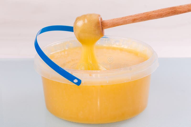 Thick Honey on Honey Dipper Above Plastic Container with Honey Stock