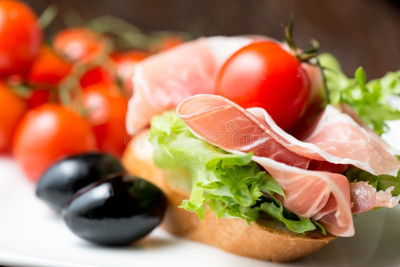 Thin Slices of Prosciutto with Olives and Tomato on Bread Stock Photo