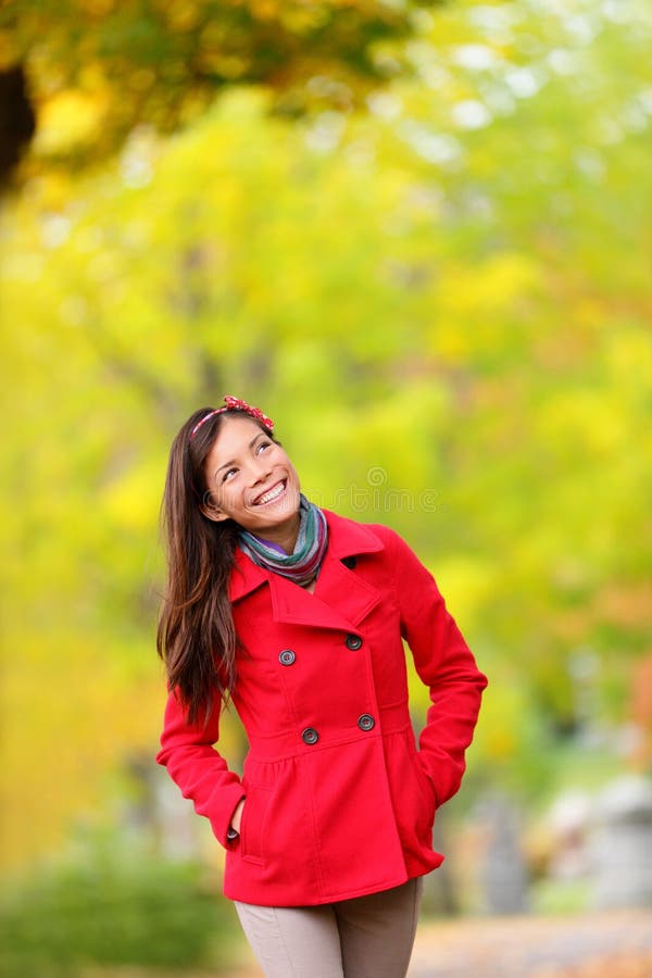 Thinking autumn woman looking up in fall forest smiling happy walking in colorful autumn foliage outdoors. Happy female model looking thoughtful at copy space outside in beautiful nature. Girl in 20s.