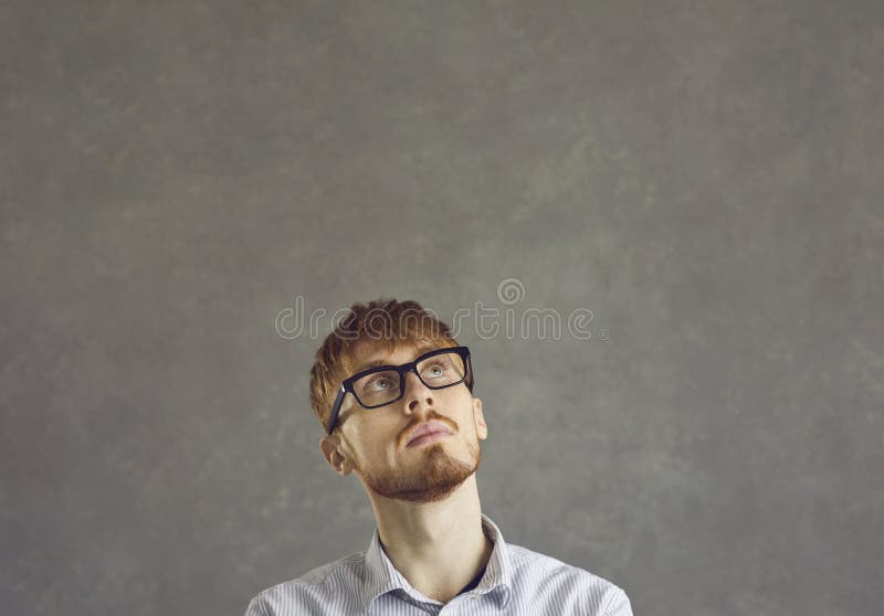 Thinking nerd man freelance programmer looking up over grey studio copy space stock image