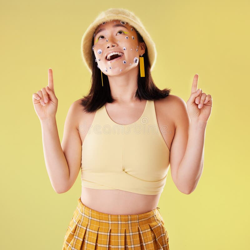 Thinking, pointing and woman with eyes for comedy isolated on a yellow background in a studio. Idea, comic and Asian stock photography