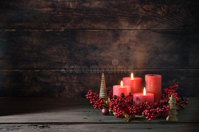 Third advent wreath with red candles, three are lit, decoration with berries, Christmas balls and small wooden trees, dark rustic