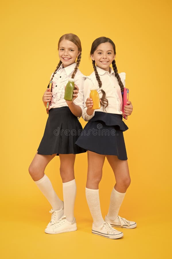 Thirst and dehydration. Healthy nutrition. Schoolgirls holding juice bottle on yellow background. Quenching thirst