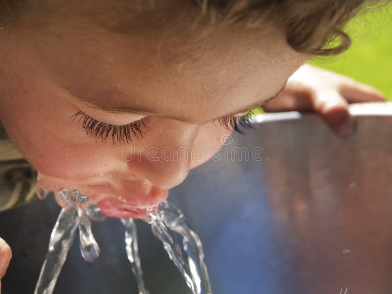 Ragazzo piccolo pendente con labbra in acqua getto di fontana.