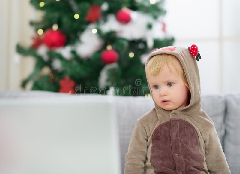 Thoughtful baby in deer suit near Christmas tree