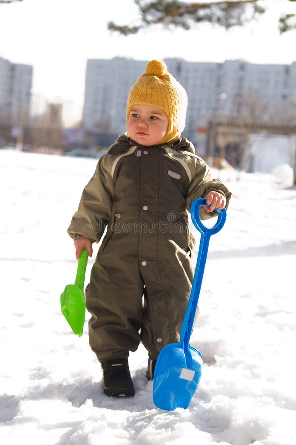 Thoughtful baby with shovels against buildings