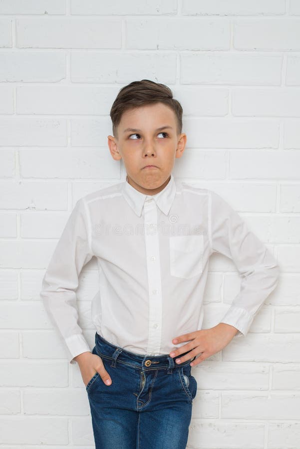 Thoughtful Boy in White Shirt and Jeans Standing Against a White Brick