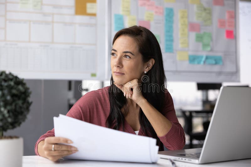 Thoughtful business woman analyzing financial report, sitting at office workplace stock photography