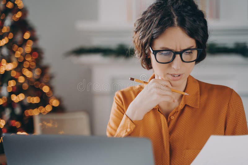 Thoughtful businesswoman in glasses working remotely from home during Christmas holidays