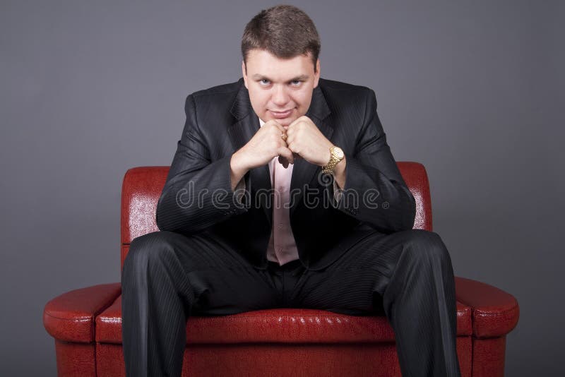 Thoughtful guy in a suit sitting on a red couch