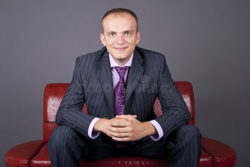 Thoughtful guy in a suit sitting on a red couch