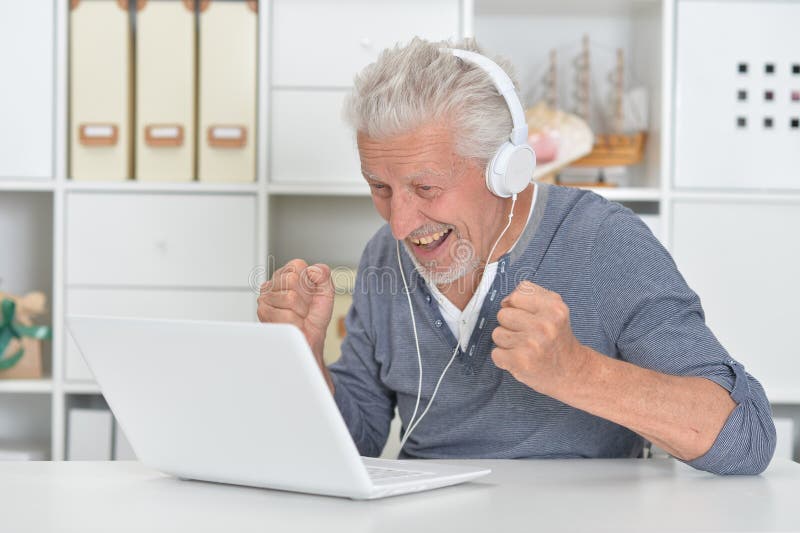 Thoughtful old man in headphones with laptop at home