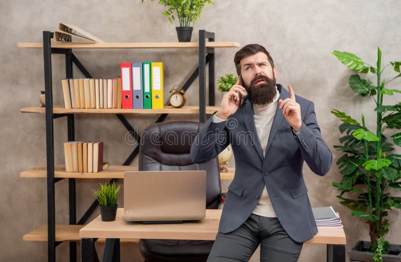 Thoughtful professional man talking on cellphone keeping finger raised in office, phone call royalty free stock images