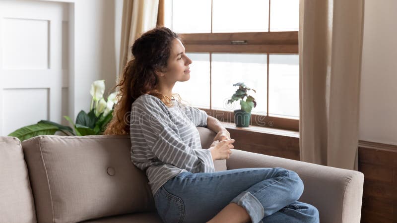 Beautiful pensive woman looking out window while resting on couch