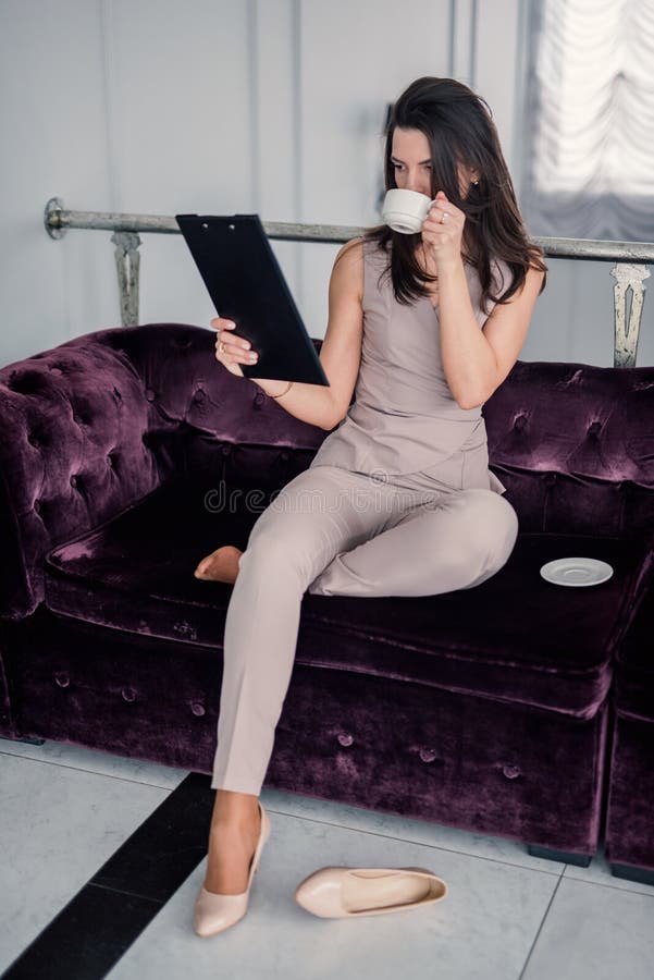 Thoughtful woman drinking coffee, using laptop and reading documents at home while sitting on the couch. copy space stock image Thoughtful woman drinking coffee, using laptop and reading documents at home while sitting on the couch. copy space stock image