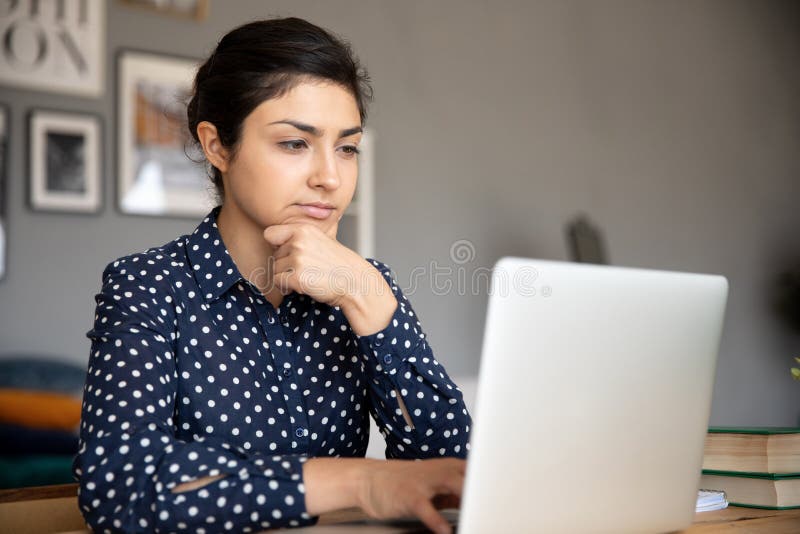 Thoughtful young indian woman looking at computer screen.