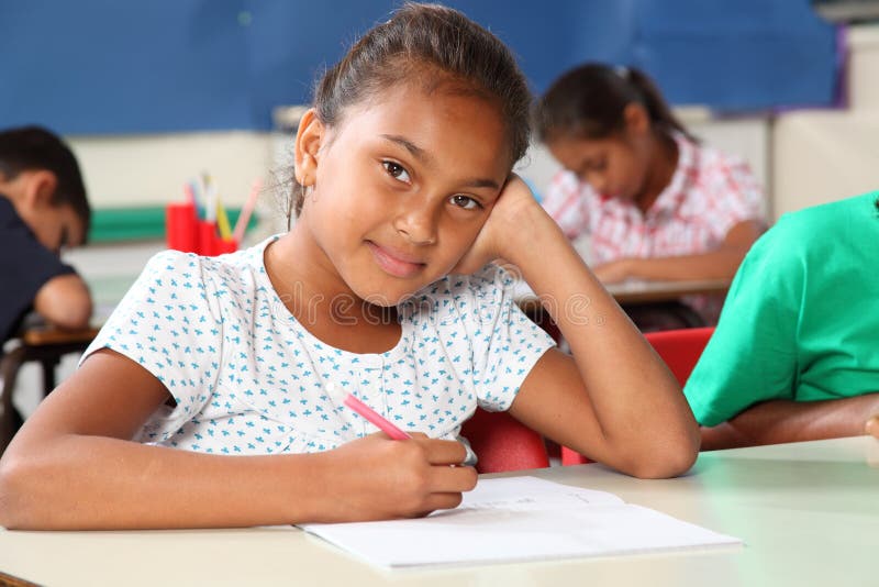Thoughtful young schoolgirl in classroom writing