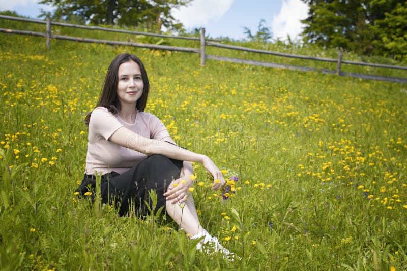Thoughtful young woman sits on a flower meadow. Summer sunny day