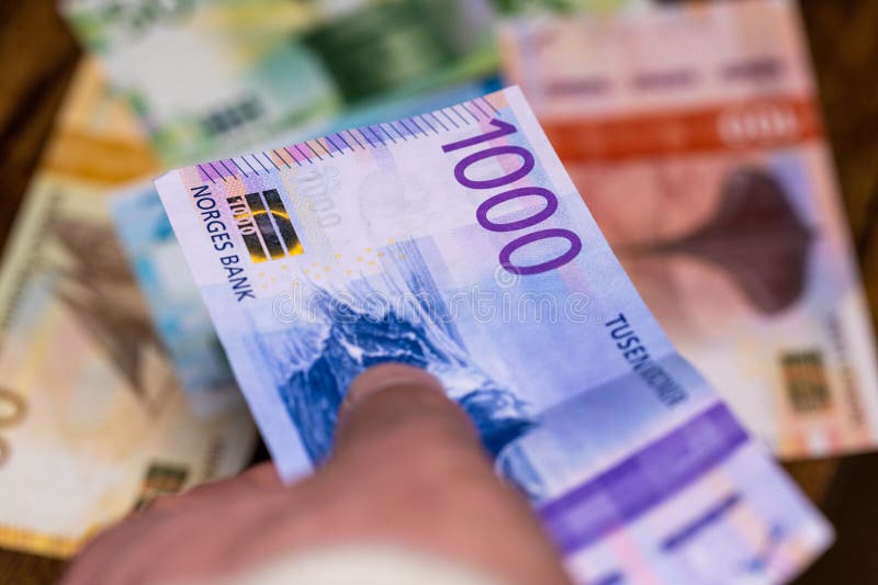 thousand norwegian kroner held in hand and put on table full of banknotes, norway currency, finance and business concept, close up, financial background