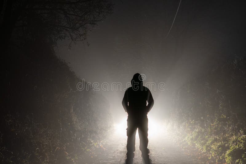 A threatening figure, standing in front of car headlights. On a country road. On a foggy winters night