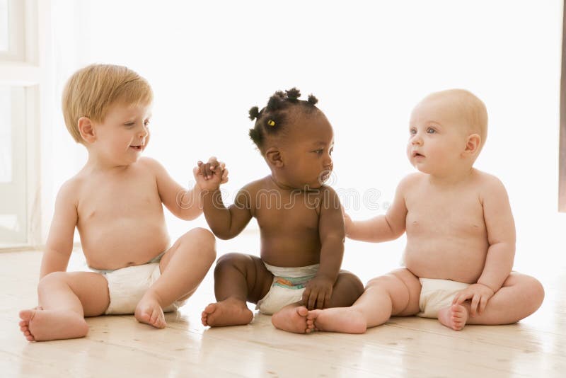 Tre bambini seduti a terra all'interno si tengono per mano.